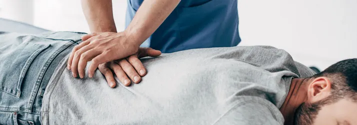Close-up of a healthcare professional performing a manual adjustment on a person lying face down on a treatment table, with hands positioned on the lower back in a clinical setting.